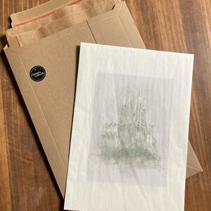 May include: A white card with a black and white drawing of a castle on it. The card is sitting on a brown paper envelope.