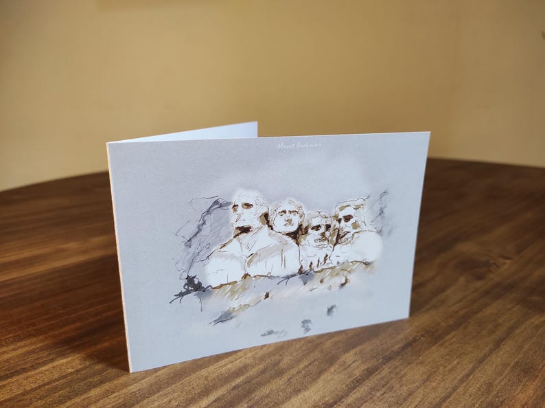 May include: A white card with a black and white ink drawing of Mount Rushmore. The drawing is a stylized interpretation of the famous monument.