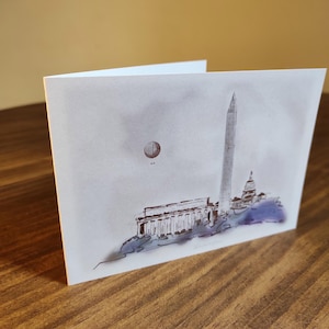 May include: A watercolor illustration of the Washington Monument and the Lincoln Memorial in Washington, D.C. A hot air balloon is in the sky above the monuments.