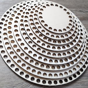 Könnte beinhalten: Ein Set aus ineinander stapelbaren, runden Holzböden in verschiedenen Größen, die jeweils eine glatte, helle Oberfläche und einen Rand mit gleichmäßig verteilten, lasergeschnittenen Löchern für Handarbeitsprojekte aufweisen.