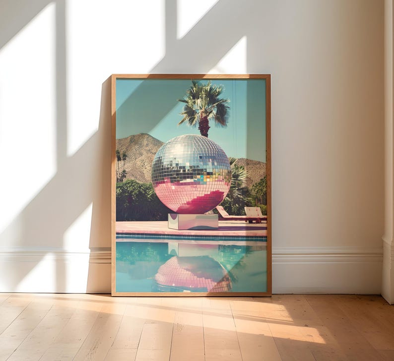 May include: A large silver disco ball sits in a swimming pool with a palm tree in the background. The pool is surrounded by a pink tiled deck.
