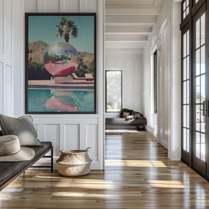 May include: A framed photograph of a large disco ball floating in a swimming pool. The disco ball is reflecting the sunlight and the pool water. The photo is hanging on a white wall in a hallway with a wooden floor.