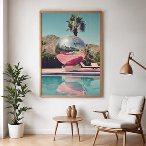 May include: A large, silver disco ball sits in a swimming pool with a palm tree in the background. The pool is surrounded by a pink patio and the disco ball is reflecting the blue sky and palm tree.