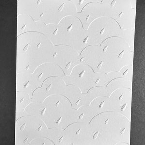 May include: White card stock with an embossed pattern of clouds and raindrops. The pattern is repeated throughout the card.