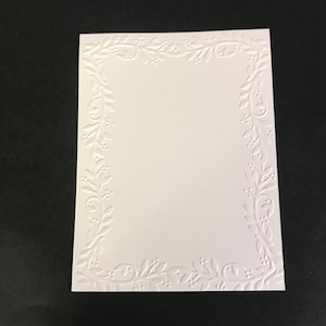 May include: White card with a raised, embossed border of leaves and vines. The border is a delicate floral design.