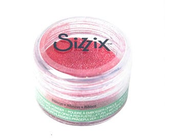 May include: A small clear jar with a red glitter powder inside. The jar has a black label with the word "Sizzix" and the text "Hibiscus - Hibiscus - Hibisco" on it.