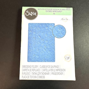 May include: A blue embossing folder with a floral design. The folder is labeled "Sizzix Textured Impressions" and "A6".