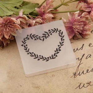 May include: Clear plastic stamp with a heart-shaped wreath design. The wreath is made of leaves and small hearts.