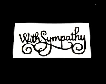 May include: A black, cursive "With Sympathy" sentiment on a white rectangular background. The text has decorative swirls and flourishes. The background is a solid black.