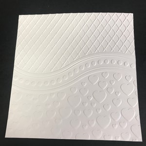 May include: White embossed paper with a repeating pattern of hearts and a wavy line with a row of circles. The top portion of the paper has a repeating diamond pattern.