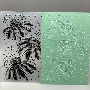 May include: A rectangular plastic embossing folder featuring a black line art design of three coneflower blossoms with swirling accents and dots, alongside a light green cardstock sheet embossed with the same floral pattern in relief.