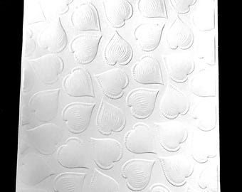 May include: A white paper sheet with a repeating pattern of embossed heart and teardrop shapes. The raised designs create a textured surface, with the shapes arranged in a grid-like layout. The image is in black and white.