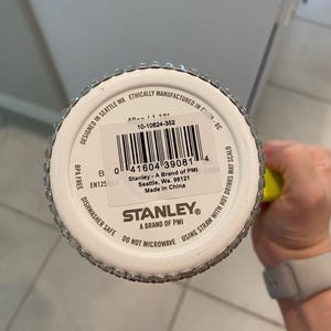 May include: A white Stanley brand tumbler with a silver rim and a barcode. The bottom of the tumbler has the text "Dishwasher Safe" and "Do Not Microwave". The tumbler is designed in Seattle, WA.