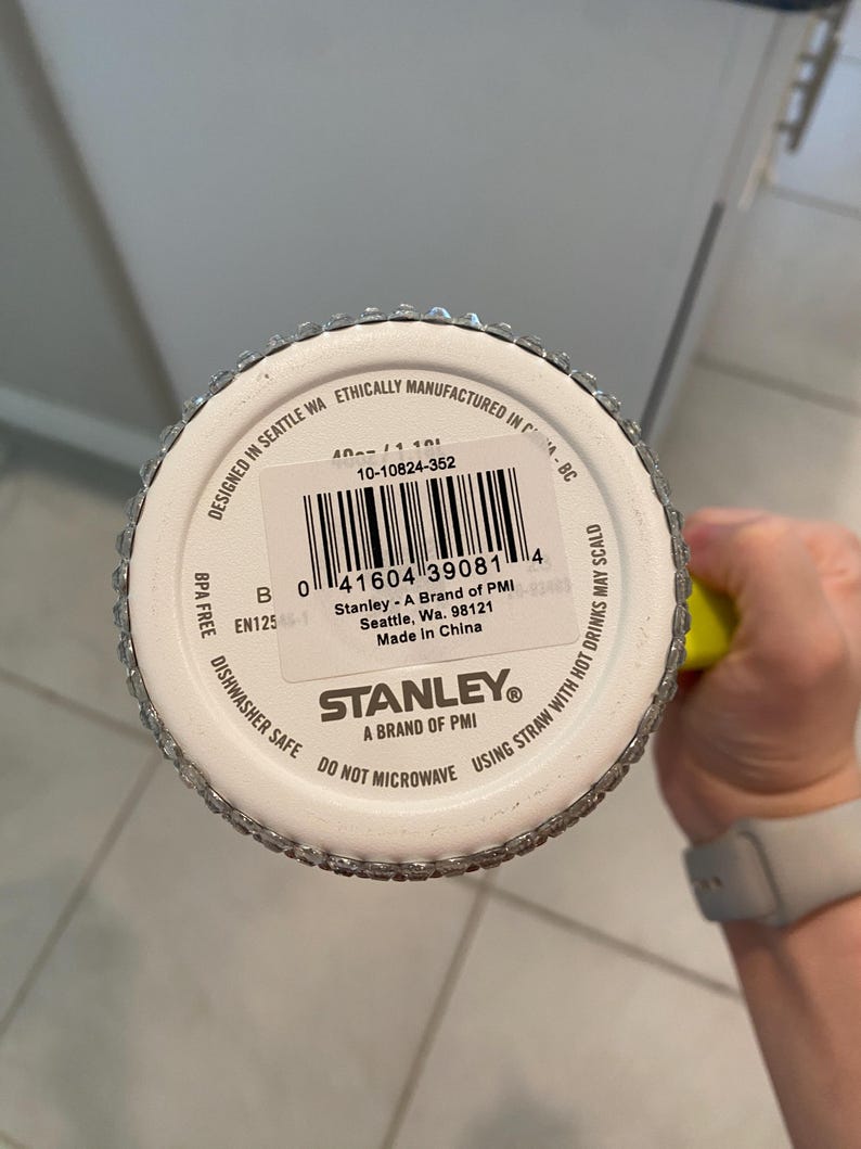 May include: A white Stanley brand tumbler with a silver rim and a barcode. The bottom of the tumbler has the text "Dishwasher Safe" and "Do Not Microwave". The tumbler is designed in Seattle, WA.