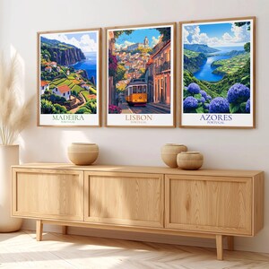 May include: Three framed travel art prints depicting scenic views of Madeira, Lisbon, and Azores, Portugal. The prints are in wooden frames and displayed above a wooden cabinet. The Madeira print shows a coastal landscape, Lisbon features a yellow tram, and Azores showcases blue hydrangeas.