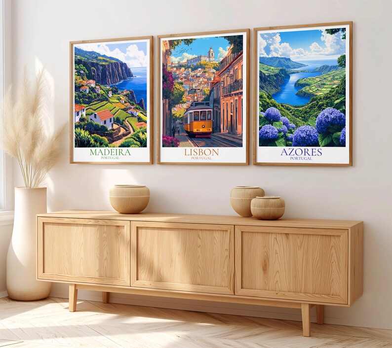 May include: Three framed travel art prints depicting scenic views of Madeira, Lisbon, and Azores, Portugal. The prints are in wooden frames and displayed above a wooden cabinet. The Madeira print shows a coastal landscape, Lisbon features a yellow tram, and Azores showcases blue hydrangeas.