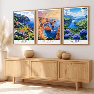 May include: Three framed landscape art prints featuring coastal scenes from Portugal. The prints showcase Madeira, Algarve, and Azores, with vibrant colors and detailed depictions of cliffs, ocean, and flowers. The frames are a light brown color.