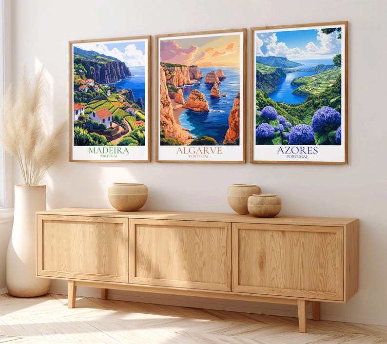 May include: Three framed landscape art prints featuring coastal scenes from Portugal. The prints showcase Madeira, Algarve, and Azores, with vibrant colors and detailed depictions of cliffs, ocean, and flowers. The frames are a light brown color.