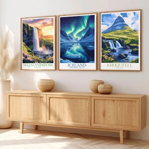 May include: Three framed landscape art prints depicting Icelandic scenery, including waterfalls and the aurora borealis. The prints are in wooden frames and are displayed above a wooden cabinet. The prints have the text "Seljalandsfoss", "Iceland", and "Kirkjufell".