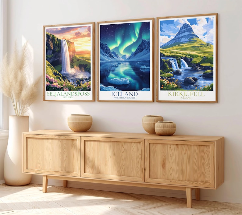 May include: Three framed landscape art prints depicting Icelandic scenery, including waterfalls and the aurora borealis. The prints are in wooden frames and are displayed above a wooden cabinet. The prints have the text "Seljalandsfoss", "Iceland", and "Kirkjufell".