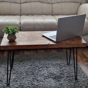 May include: A rectangular wooden coffee table with a dark stain finish. The table has black hairpin legs and a small potted plant. A silver laptop is on the table. The table is approximately 100 cm long.