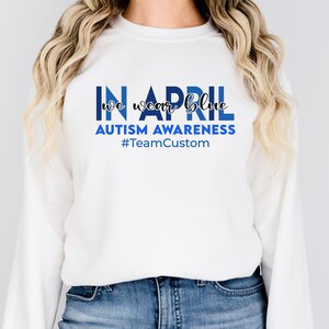 May include: White sweatshirt with the text "IN APRIL we wear blue" in blue block letters and script. Below the text is "AUTISM AWARENESS" and "#TeamCustom" in blue.