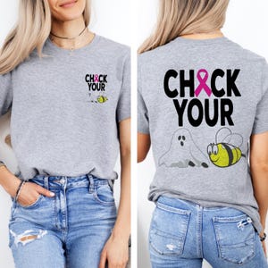 May include: A heather gray t-shirt with the text "CHECK YOUR" in black and a pink ribbon. The shirt features a cartoon ghost and a bee. The front of the shirt has the same text and bee.