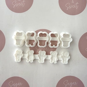 May include: A selection of white plastic cookie cutters shaped like teddy bears and ice cream cones. The image features the text "Sugar & Sweet" in a circular design. The cutters are displayed on a white surface.
