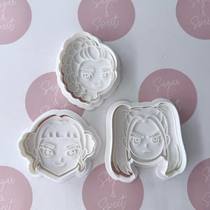 May include: Three white plastic cookie cutters, each featuring a distinct anime-style character face. One cutter shows a character with a braided hairstyle, another with a bob cut, and the third with high pigtails, all with detailed facial features.