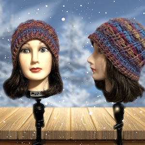 Puede incluir: Un gorro de punto con un ajuste holgado en un hilo multicolor con tonos de azul, morado, rojo y marrón. El gorro se muestra en una cabeza de maniquí sobre un fondo nevado.