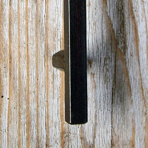 May include: Black metal door handle with a hexagonal shape. The handle is mounted on a light wood surface.