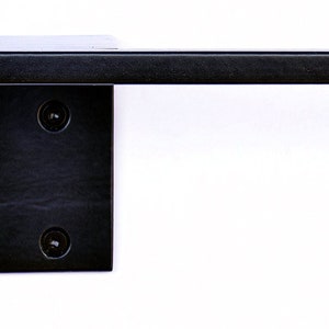 May include: Black metal toilet paper holder with a square design. The holder is mounted to the wall with two screws.