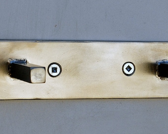 Puede incluir: Un toallero de pared de metal plateado cepillado con dos ganchos de metal negro. El toallero tiene dos pequeños agujeros redondos en la parte delantera.