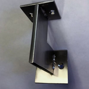 May include: A stainless steel bracket with a right-angle design. The bracket features a rectangular base with two pre-drilled holes and a vertical support piece welded to it. The metal has a brushed finish.