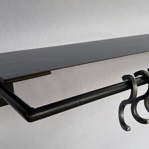 May include: Black metal shelf with a black metal rod and five hooks. The shelf is mounted to a wall.