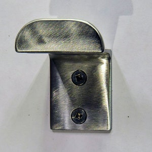 May include: A brushed silver metal hook with two screws. The hook is designed to be mounted on a wall.