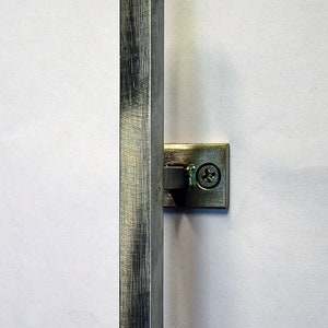 May include: A metal cabinet pull with a brushed finish. The pull is a long, hexagonal bar attached to a small, square mounting plate with a single screw. The hardware is a muted silver color.