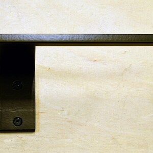 May include: Black metal toilet paper holder mounted on a wall. The holder has a rectangular base and a curved arm.