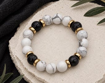 May include: A beaded bracelet featuring alternating white marble-patterned beads and solid black beads, accented with small, polished gold-tone metal spacers arranged in a circular pattern to form a continuous loop of round, smooth gemstone-style beads.