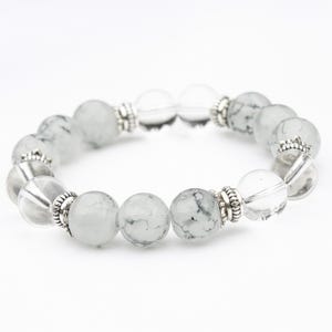 May include: A beaded bracelet featuring clear and gray-toned round beads. The beads are interspersed with silver-colored metal accents. The bracelet is displayed against a white background, highlighting its design and materials.