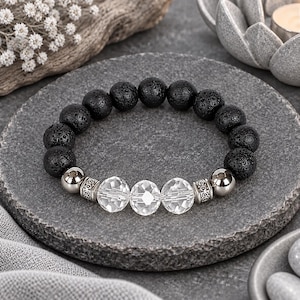 May include: A beaded bracelet featuring a series of porous black lava stone beads, three clear faceted crystal beads in the center, and two smooth metallic silver-toned spheres flanked by decorative engraved silver-toned metal spacers.