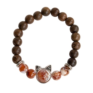 May include: A beaded bracelet featuring dark brown wooden beads and orange and white patterned stone beads. A silver-toned cat-shaped charm with a central orange stone adds a unique accent to the bracelet.