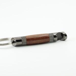 May include: A silver bottle opener with a wooden handle attached to a silver key ring. The bottle opener has a textured metal finish.