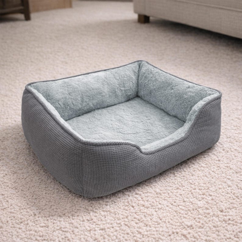 May include: A gray pet bed with a soft, plush interior and a textured exterior. The bed has a rectangular shape with raised sides for added comfort and security. The interior is a light blue-gray color.
