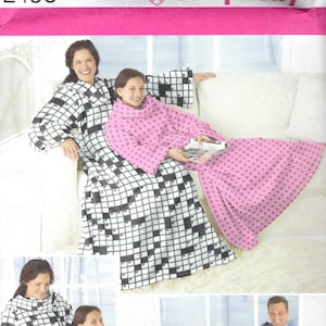 May include: Simplicity pattern 2490 featuring wearable blankets. The image shows a woman and a girl wearing a black and white crossword-patterned blanket and a pink blanket with a small square pattern. A man is wearing a blue blanket with a deer pattern.