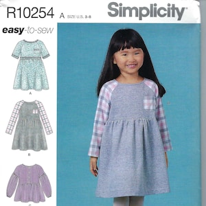 May include: Simplicity sewing pattern number R10254 for girls' dresses and pants. The pattern includes four different styles: a teal floral dress, a gray dress with plaid sleeves, a purple dress with puffed sleeves, and floral pants. The pattern is for sizes 3-8.