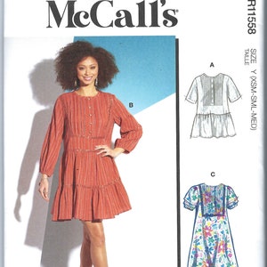 Könnte beinhalten: Ein Schnittmuster für ein Kleid mit drei verschiedenen Ansichten. Das Kleid ist in einem rot-weiß gestreiften Stoff, einem weißen Stoff und einem Blumenstoff gezeigt. Das Schnittmuster enthält Anweisungen zum Nähen des Kleides. Das Schnittmuster ist für die Größen XS, S und M.
