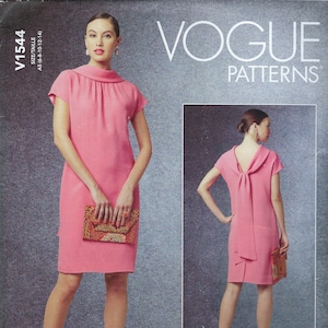 Könnte beinhalten: Vogue Patterns V1544 Schnittmuster mit einem rosa Kleid mit hohem Ausschnitt und kurzen Ärmeln. Das Schnittmuster enthält eine Rückansicht des Kleides mit Schleifendetail. Das Model hält eine gemusterte Clutch. Der Text "VOGUE PATTERNS" ist sichtbar.