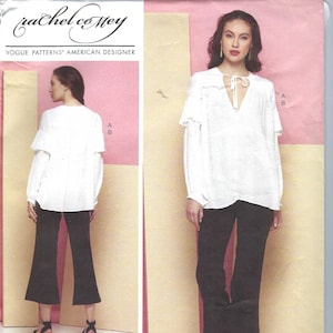 Può includere: Una blusa bianca con scollo a volant e maniche lunghe. La blusa ha un nodo al collo. La modella indossa pantaloni neri e sandali.