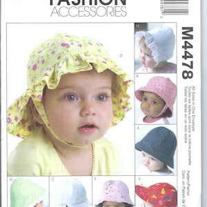 May include: McCall's Fashion Accessories pattern M4478. The image shows a baby wearing a yellow floral sun hat with a ruffled brim. Other hats include a pink dotted hat, a blue hat, and a red hat with colorful designs.